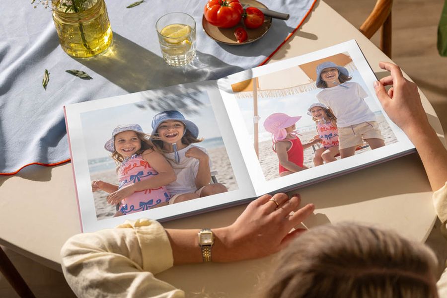 En öppen fotobok på ett köksbord visar bilder av unga flickor som har roligt på stranden, som illustrerar önskefotos tips om att blicka tillbaka på sommarminnen med en personlig fotobok.