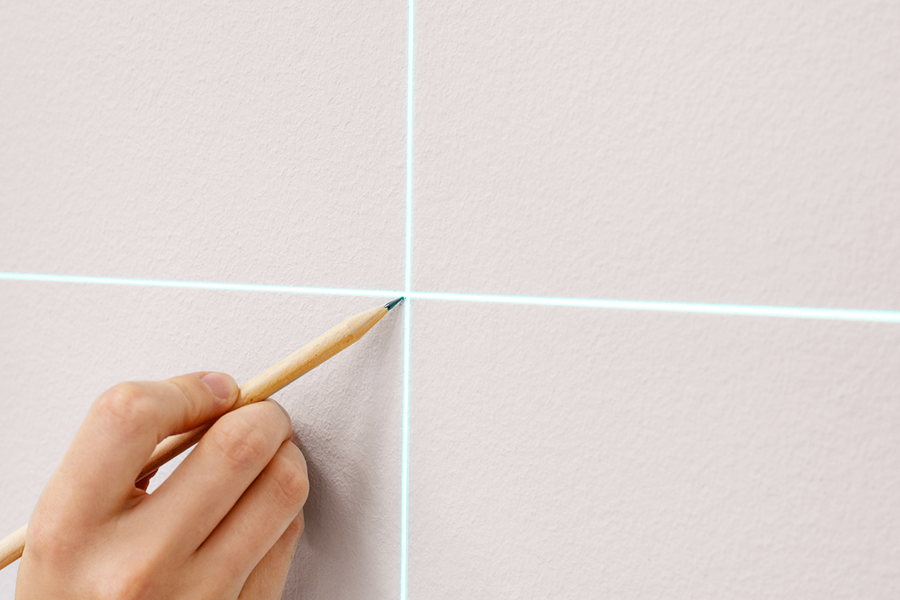 En hand markerar en vägg som förberedelse för att hänga upp väggkonst, vilket illustrerar önskefotos steg-för-steg-tips om att markera väggen innan man installerar ett ramupphängningskit.