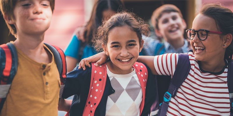 Tre skolkompisar kramar varandra och ler mot kameran, som fångar glädjen inför första dagen i skolan i önskefotos guide till fantastiska skolfoton.