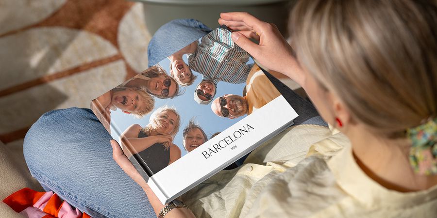 En kvinna tittar på en fotobok med titeln 'Barcelona', med en bild av många leende familjeansikten som tittar ner i kameran, vilket illustrerar önskefotos guide till att skapa en gruppfotobok från semestern.