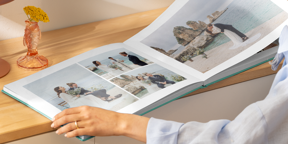 En kvinnas händer håller upp en uppslagen bröllopsfotobok med en dubbelsida med olika strandbilder på en brud och en brudgum, som illustrerar önskefotos idéer till titlar på bröllopsfotoboken.