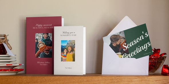 Fotokort i vinrött, grått och grönt på en trähylla, ett i ett vitt kuvert