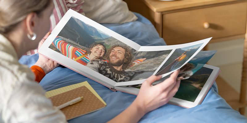 önskefoto fotobok-inspiration: En kvinna tittar i en öppen fotobok med ett dubbeluppslag som visar ett par i ett bergslandskap.