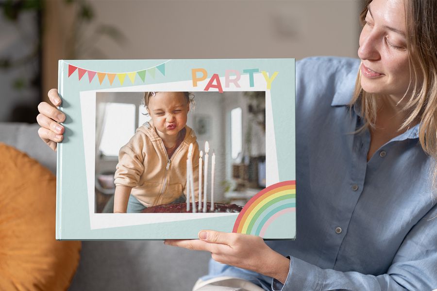 A woman holding up a party-themed birthday photo book from Photobox with a child blowing out candles on the cover, perfect for a 1st birthday photo book or birthday photobooks.