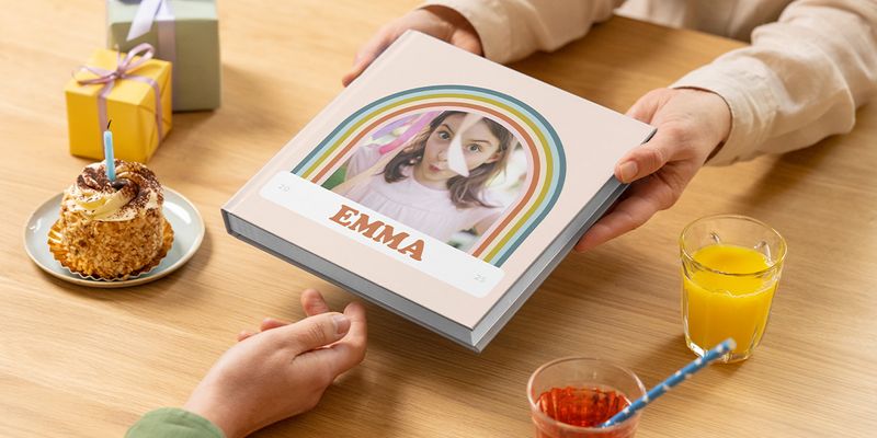 En fotobok födelsedag för Emma räcks över ett bord med tårta och present, vilket visar en personlig födelsedagspresent eller fotobok födelsedag hos önskefoto.