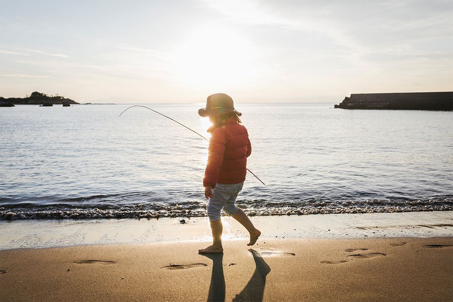 Ett barn står på stranden vid havet med en tydlig skugga bakom sig, och illustrerar den dramatiska effekten av silhuettfotografering i solljus.