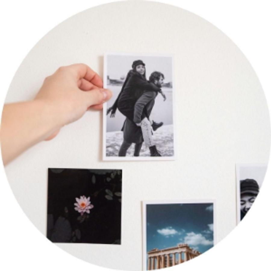 En hand håller ett fotoprint av ett par bredvid andra fotoprintar, som illustrerar Andreas frieriberättelse och en minnesfylld och betydelsefull frieriidé från önskefoto.