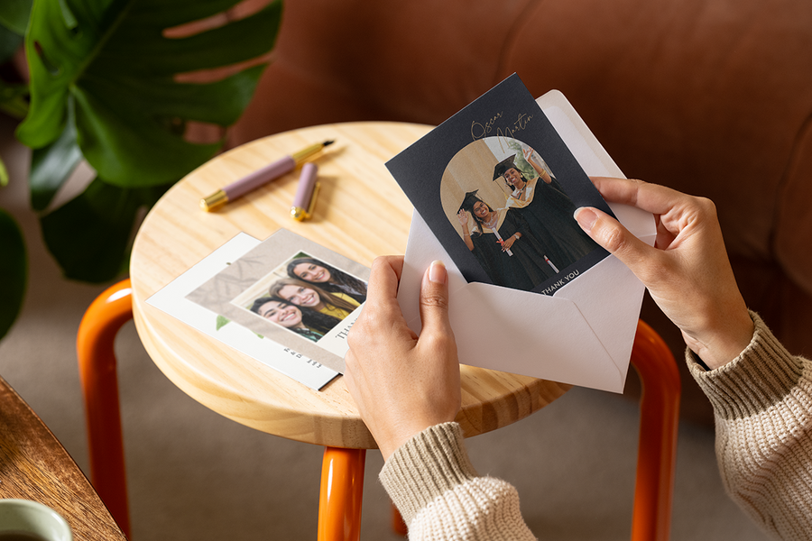 Händer stoppar ner ett personligt önskefoto tackkort till en lärare med en bild av studenter på framsidan i ett kuvert.