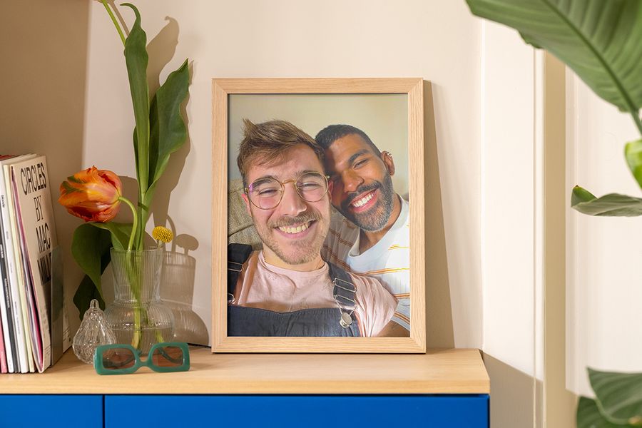 Ett inramat foto av två män som tar en selfie i solen står på en skänk bredvid en vas, solglasögon och ett magasin, som inspiration till sommardekoration och somrig inredning.