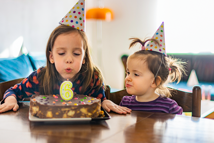 En flicka i kalashatt blåser ut ljuset på sin 6-årstårta tillsammans med en vän, vilket ger tips på en personlig födelsedagspresent till barn från önskefoto.