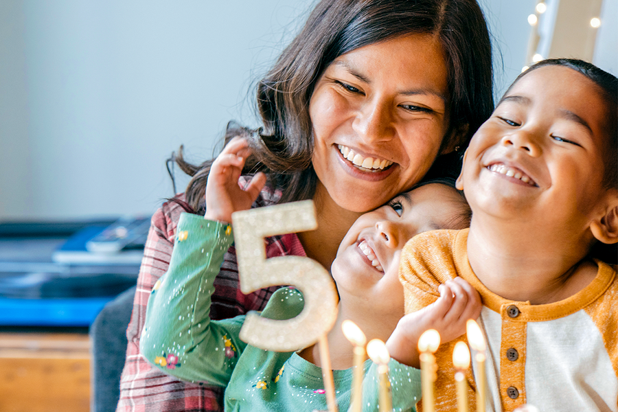 En mamma och hennes två barn ler bredvid en tårta till 5-årsdagen, vilket visar en personlig födelsedagspresent och presenttips från önskefoto.