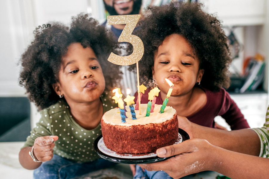Två tvillingflickor som ska blåsa ut ljusen på sin 3-årstårta, vilket ger tips på en födelsedagspresent och personlig födelsedagspresent från önskefoto.