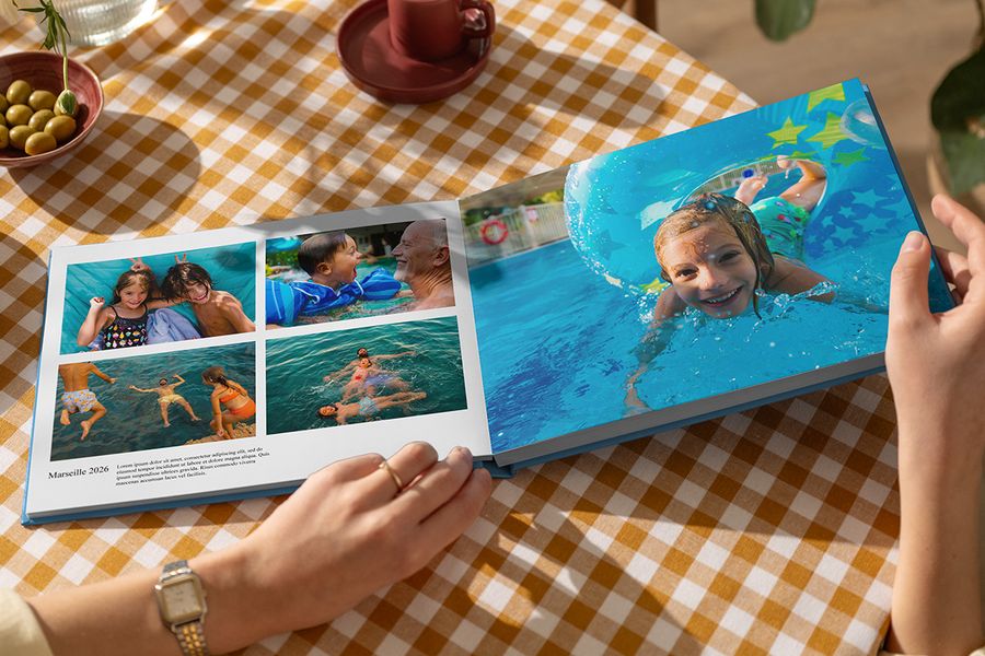 En öppen önskefoto semesterbok visar familjens sommarbilder från lek i vattnet, med ett stort uppslag och en annan sida med titeln Marseille 2026, bildtext och beskrivning, vilket illustrerar hur texter ger liv åt en personlig fotobok resa.