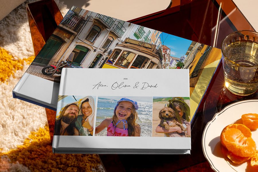 Två olika önskefoto resefotoböcker visas tillsammans, bland annat en liggande fotobok resa med familjens resebilder på omslaget och en annan med en semesterbild av en spårvagn, som inspiration till olika typer av fotoalbum travel.