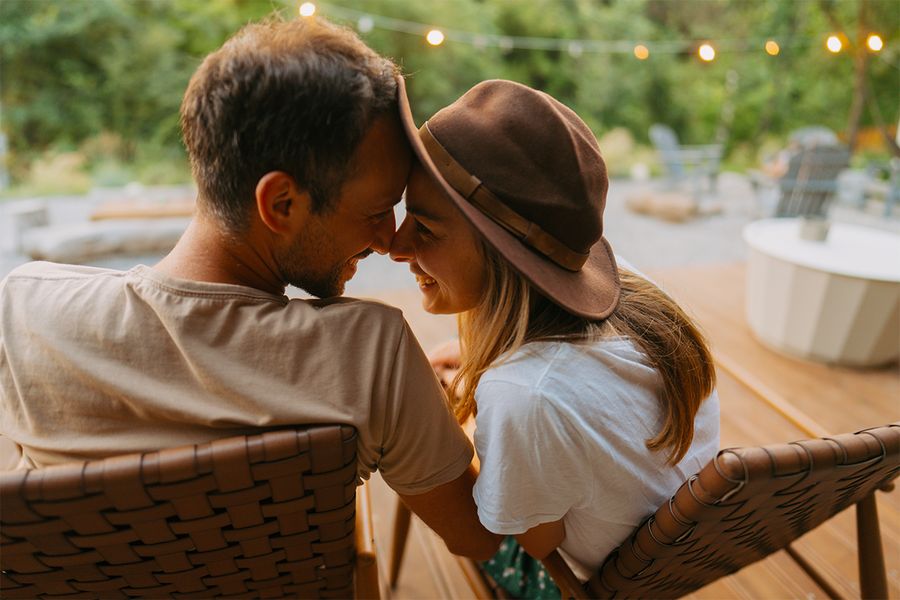 En man och en kvinna sitter kärleksfullt tätt intill varandra i en trädgård utsmyckad med ljusslingor, ett romantiskt ögonblick från önskefotos staycation-idéer för par.