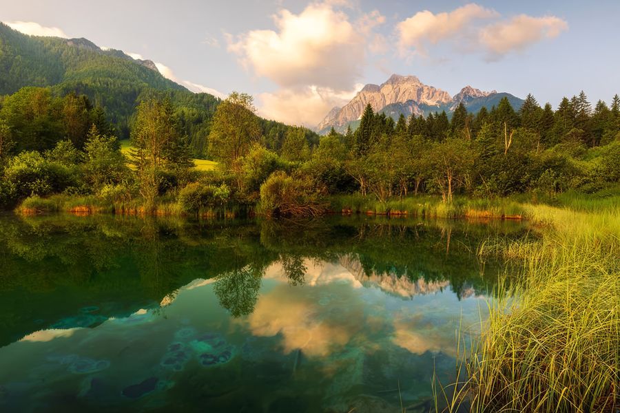 Höga kalkstenstoppar och det klara, speglande vattnet i sjön Bohinj i Triglavs nationalpark i Slovenien, en av Europas bästa nationalparker i önskefotos guide.