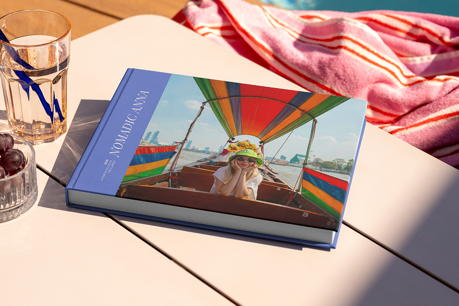 En stor liggande resefotobok med titeln 'Nomadic Anna' ligger på ett bord, med en bild av en tjej på resande fot på omslaget, som illustrerar önskefotos fotobok titel idéer för resor.