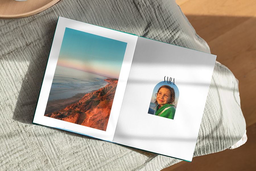 En öppen fotobok visar ett vackert landskap på en sida och en bild av en flicka med bildtexten 'Sara' på den andra, vilket illustrerar önskefotos Artisan Masking-design med lekfulla ramar inspirerade av vintage vykort och frimärken.