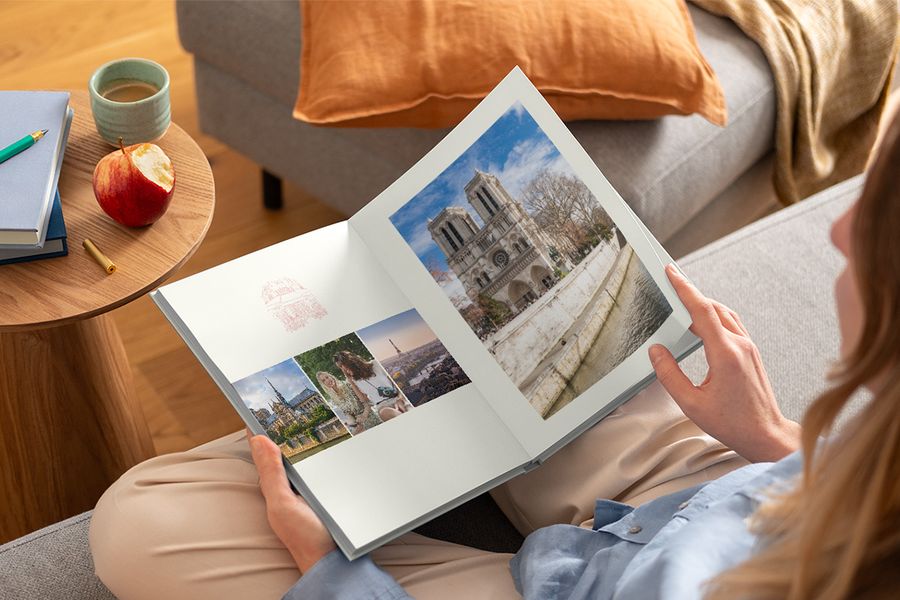 En kvinna håller en öppen fotobok i knät med olika resebilder, vilket illustrerar önskefotos Graphic Getaways-design inspirerad av vintage reseaffischer och illustrerade stadskartor.