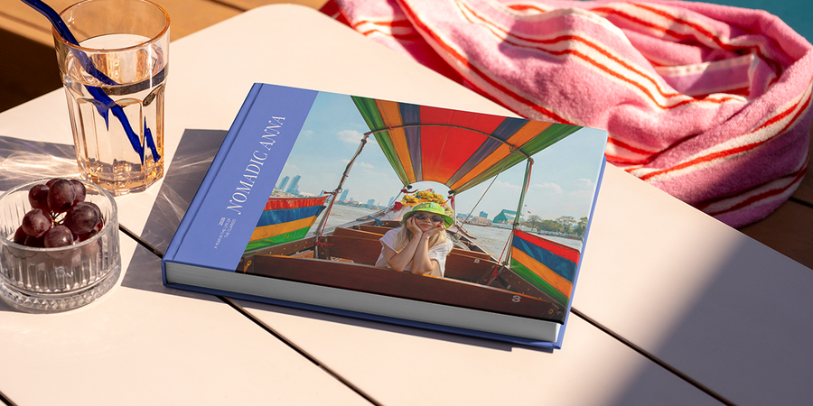 En stor liggande resefotobok med titeln 'Nomadic Anna' ligger på ett bord, med en bild av en tjej på resande fot på omslaget, som illustrerar önskefotos fotobok titel idéer för resor.