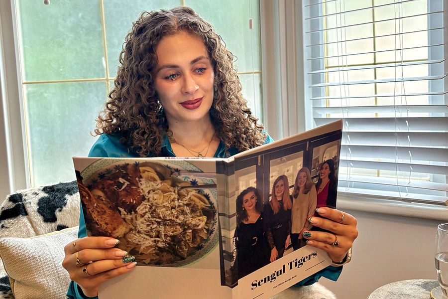 Sarah, som arbetar på önskefoto, sitter i en kostoppad stol och tittar på sin personliga familjekokbok, vars omslag visar fyra kvinnor, inklusive Sarah själv, vilket illustrerar hur en receptfotobok samlar familjerecept och minnen.
