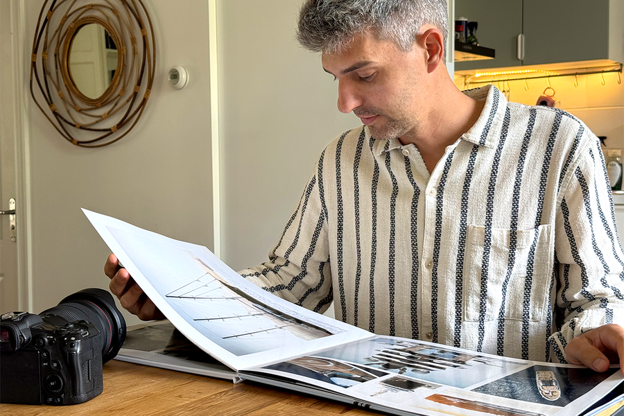 Charl van Rooy sitter i sitt kök och tittar ner på sin öppna portfolio, med sin kamera bredvid sig på bordet, vilket illustrerar önskefotos guide till att skapa en fotografiportfolio som fotobok.
