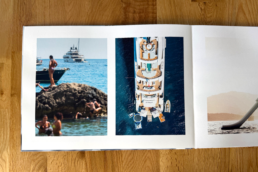 Ett öppet uppslag från Charl van Rooys fotobok visar semesterscener på stranden, med folk som slappnar av vid havet och en yacht, vilket illustrerar det visuella flödet i hans fotografiportfolio.
