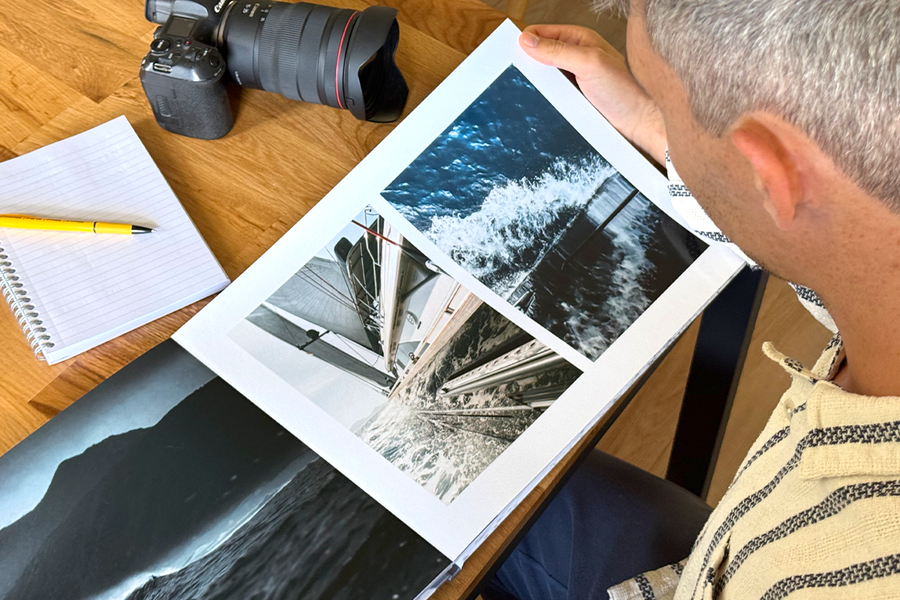 Fotografen Charl van Rooy tittar ner på sin portfolio, med sin kamera och en anteckningsbok på bordet bredvid honom, vilket illustrerar önskefotos tips för att välja de bästa mallarna och layouterna för en fotografiportfolio.