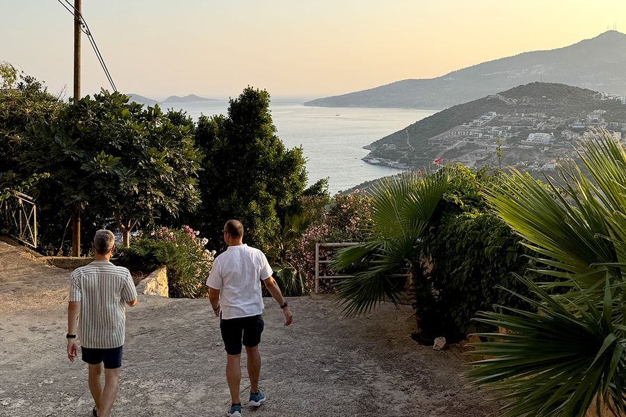 Två män går ner för en kulle omgiven av växter mot havet i Kalkan, vilket fångar charmen med en turkisk septembersemester vid Turkosa kusten.
