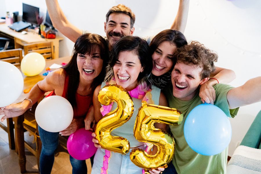 En grupp unga människor samlas kring ballonger med siffran '25', ler och poserar för en bild, vilket illustrerar önskefotos tips för att fånga stora födelsedagsögonblick.