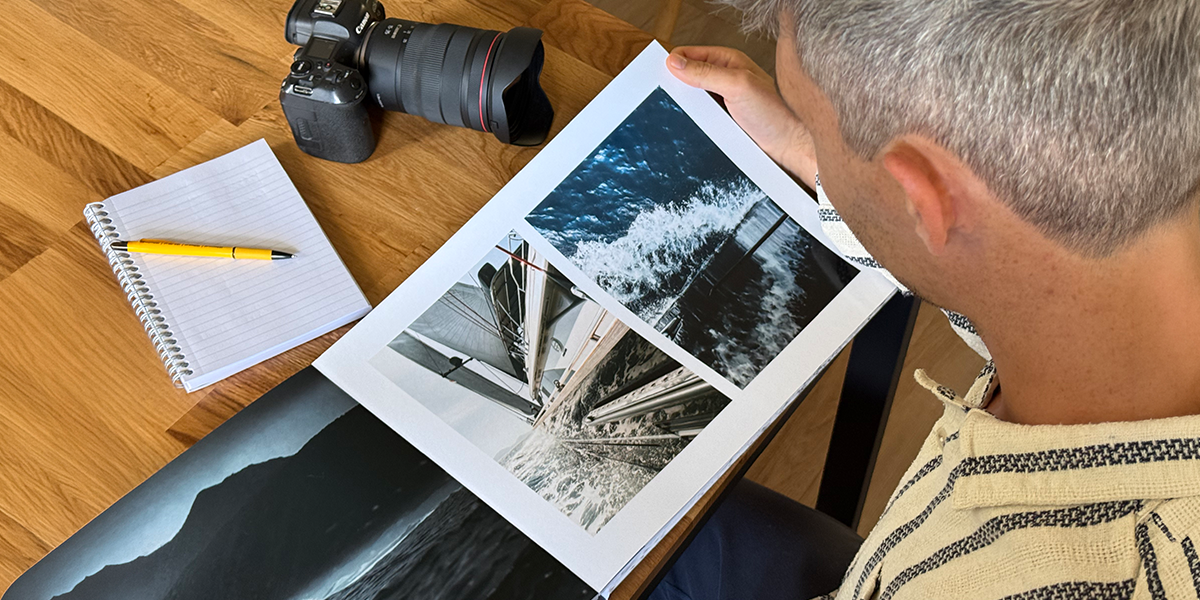 Fotografen Charl van Rooy tittar ner på sin portfolio, med sin kamera och en anteckningsbok på bordet bredvid honom, vilket introducerar önskefotos guide till att skapa en fotografiportfolio som fotobok.