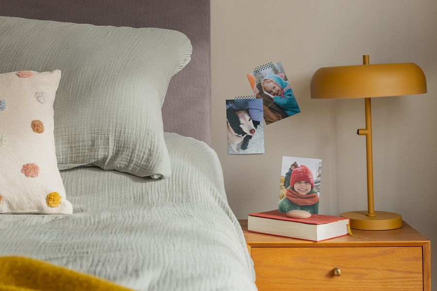Ett urval familjefotoutskrifter hänger på väggen bredvid en säng, vilket illustrerar hur önskefotos fotoutskrifter ger en mysig och personlig touch åt ett hygge-sovrum.