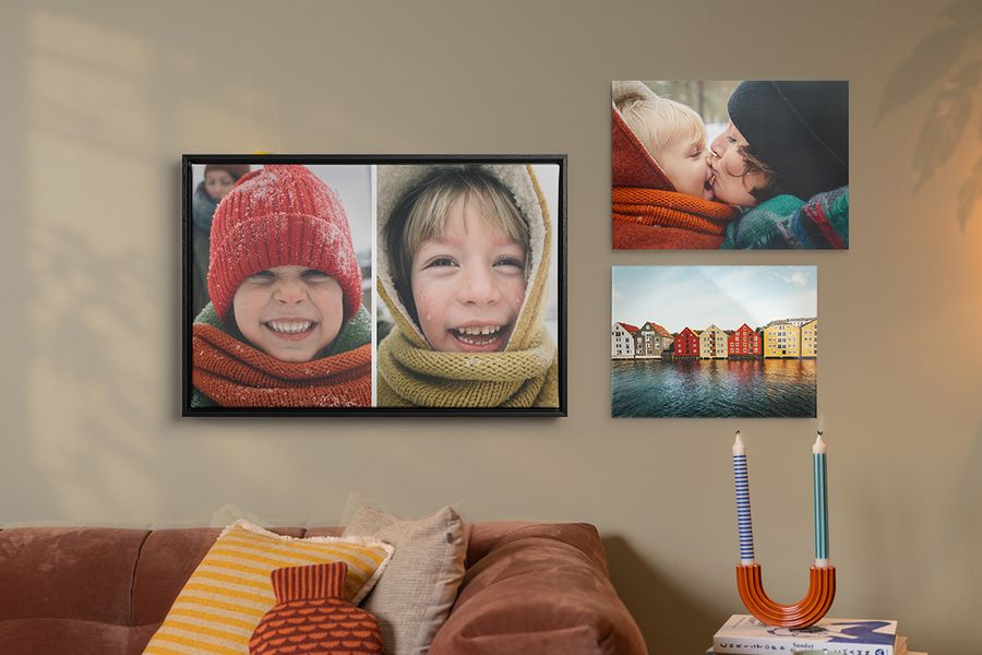 Tre exempel på personlig väggkonst hänger ovanför en soffa i ett vardagsrum, höstiga familjebilder med leende barn i vinterkläder, vilket illustrerar hur önskefotos väggkonst ger en mysig hygge-stil åt hemmet.