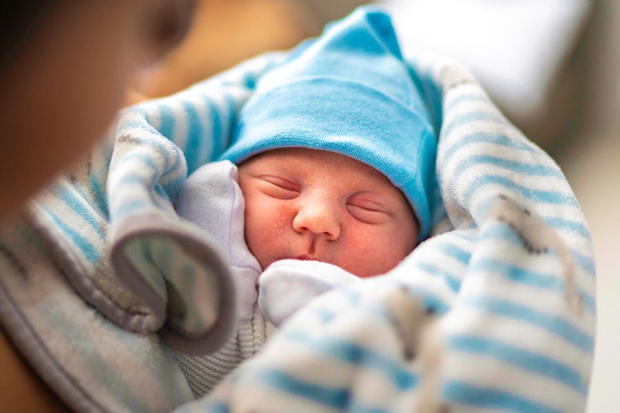 Nyfödd bebis tätt inbäddad i en blå- och vitrandig filt med blå mössa, som illustrerar önskefotos idéer för att fira bebisens första jul med något personligt.