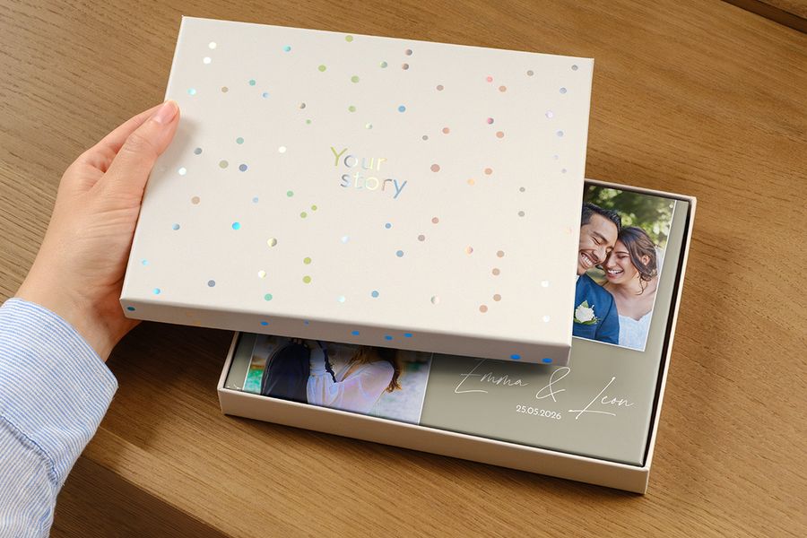 En bröllopsfotobok ligger i den nya presentationsboxen, med en bild av paret och bröllopsdatumet som titel på omslaget, delvis dolt av presentboxens öppna lock, vilket illustrerar varför en presentationsbox är värd det för en premium bröllopsfotobok.
