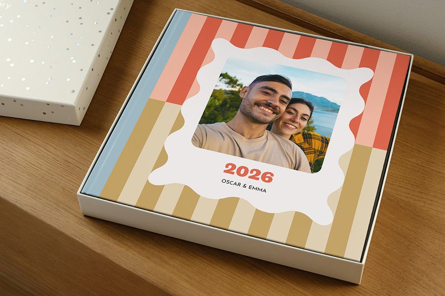 En fotobok ligger i presentboxen utan locket, och ser ut som en årsbok märkt '2026' med ett leende par på omslaget, vilket illustrerar hur man väljer rätt storlek på presentationsbox till sin fotobok.