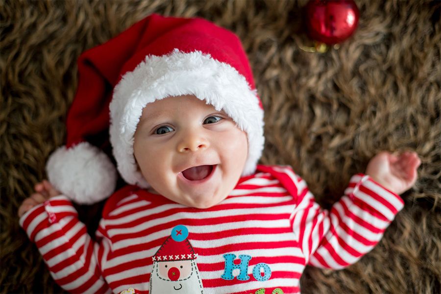 Leende bebis på en matta med tomteluva och en röd- och vitrandig jultröja, som illustrerar önskefotos tips för att ta julfoton av bebisens första jul.