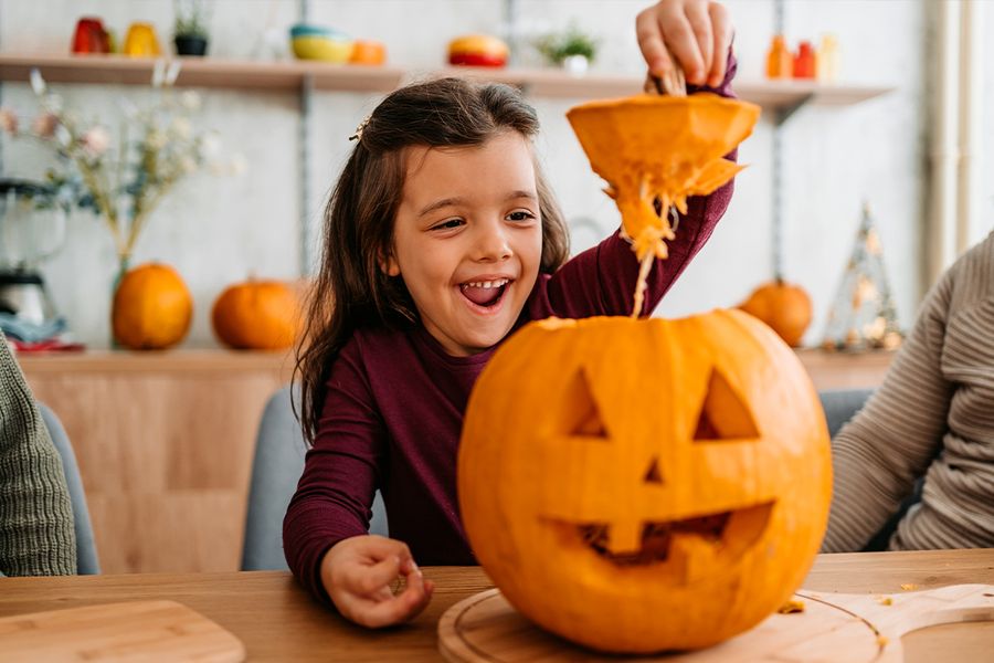 Ett barn lyfter av toppen på en pumpa som det precis har skurit ut, vilket illustrerar önskefotos roliga och gulliga pumpacitat för Halloween-bildtexter på Instagram.