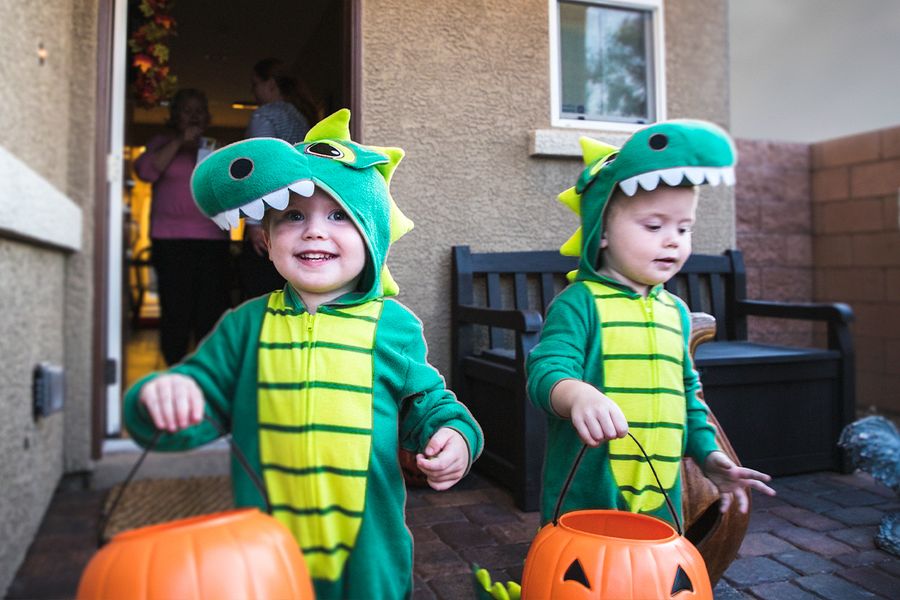Två små pojkar i dinosauriekostymer går och gör bus eller godis med pumpakorgar i händerna, vilket illustrerar önskefotos Halloween-citat för bilder från bus eller godis.