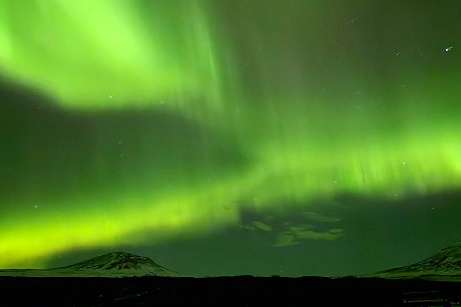 Snöklädda berg under en himmel som är så grön av norrsken, som illustrerar önskefotos tips om var man kan se norrsken utan att åka till Island.