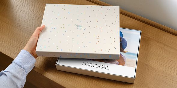 En önskefoto presentationsbox står med locket på glänt, och visar en personlig resefotobok för Portugal inuti, med omslaget delvis dolt av locket, vilket introducerar önskefotos nya fotobok-presentbox.
