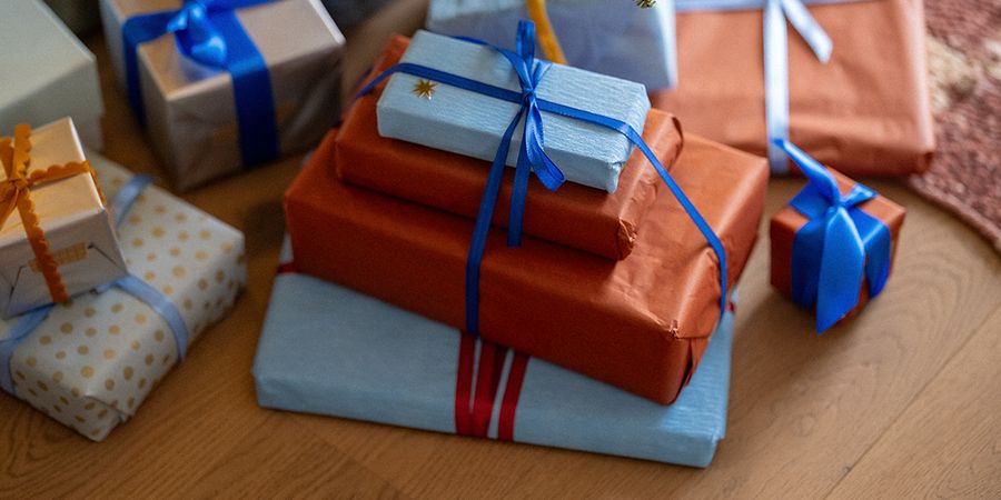 En hög med presenter inslagna i orange och ljusblått papper och knutna med blå band på ett trägolv, som illustrerar önskefotos tips för black friday julklappar.