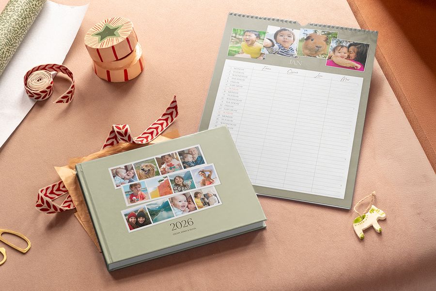 En salviagrön fotobok med 2026 på omslaget och en väggkalender för familjen med foton överst och kolumner för varje familjemedlem, som illustrerar önskefotos delbara familjekalender som Black Friday-julklapp.