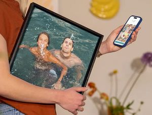 En kvinna håller sin mobil med önskefoto-redigeraren öppen medan hon bär semesterinspirerad väggdekor under armen med två män som har roligt i en pool, som inspiration för att förvandla semesterbilder till vacker väggkonst.