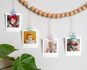 Bebisbilder fästa med klämmor på en girlang av träpärlor, upphängd på väggen.