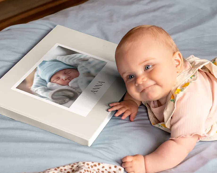 Bebis som ligger bredvid en personlig fotobok med en bebisbild på omslaget.