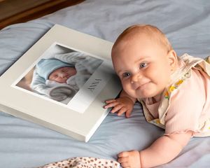 Bebis som ligger bredvid en personlig fotobok med en bebisbild på omslaget.
