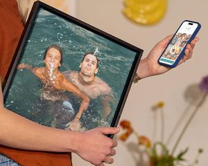 En kvinna håller önskefoto väggdekor med en familj som leker i vattnet på semestern, som inspiration för att förvandla semesterbilder till vacker väggkonst.